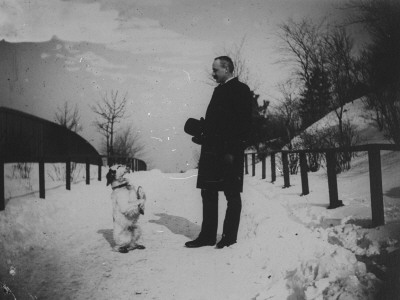 A Well-Dressed Man And His Dog Standing At Attention On A Snow-Covered Path by Wallace G. Levison Pricing Limited Edition Print image
