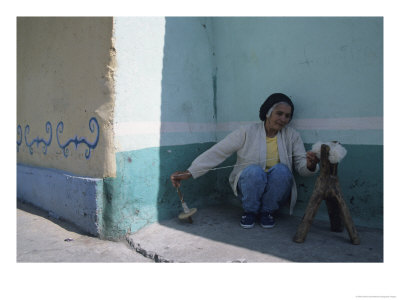 An Elderly Venezuelan Woman Spins Yarn In Front Of A Colorful Wall by David Evans Pricing Limited Edition Print image