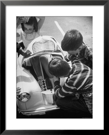 Girl Demurely Adjusting Her Hair While Willing Volunteers Repair Jammed Front Wheels Of Her Car by Nina Leen Pricing Limited Edition Print image