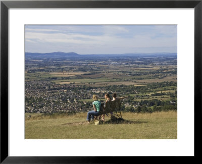 Three Girls Sitting On Bench Looking At View Over Bishops Cleeve Village, The Cotswolds, England by David Hughes Pricing Limited Edition Print image