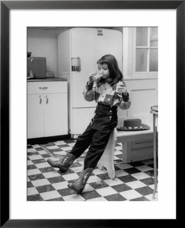 Young Girl Wearing Cowgirl Outfit Drinking Milk And Eating Sandwich In Kitchen by Nina Leen Pricing Limited Edition Print image