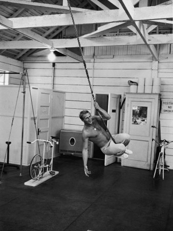 Actor Steve Mcqueen Swinging On Rope In Room With Workout Equipment by John Dominis Pricing Limited Edition Print image