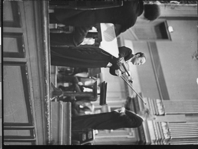 Violin Virtuoso Jascha Heifetz Holding Violin And Bow At Concert, As Conductor Works Behind Him by Alfred Eisenstaedt Pricing Limited Edition Print image