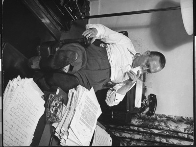Writer Damon Runyon Sitting With Feet Up At Work-Piled Desk Drinking Milk by Gjon Mili Pricing Limited Edition Print image