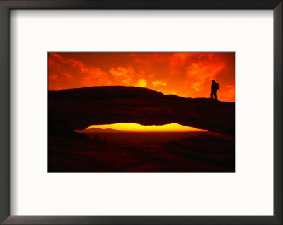 Silhouette Of A Hiker On Mesa Arch Against A Spectacular Orange Sky, Utah, Usa by Cheyenne Rouse Pricing Limited Edition Print image