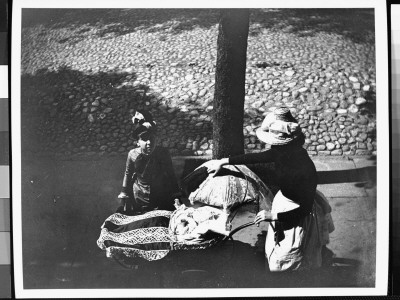 Two Women Walking With A Baby In A Carriage On A Sidewalk Next To A Cobblestone Street by George B. Brainerd Pricing Limited Edition Print image