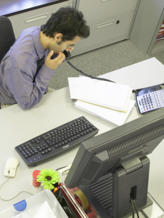 Office Life And Interiors, Office Worker On The Phone At His Desk Biting His Nails by Richard Bryant Pricing Limited Edition Print image