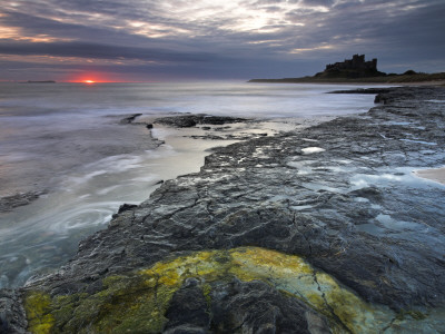 The First Glow Of Sunrise Over The Sea Beside Bamburgh Castle, Northumberland, England by Adam Burton Pricing Limited Edition Print image