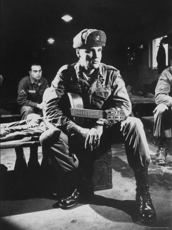 Elvis Presley Sporting Battle Fatigues As He Sits On Cot With Guitar Tucked Under His Arm by Loomis Dean Pricing Limited Edition Print image