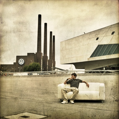 A Young Man Sitting On A Sofa Infront Of The Volkswagen Factory by Jewgeni Roppel Pricing Limited Edition Print image