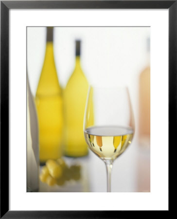 A Glass Of White Wine And Wine Bottles In Background by Ulrike Koeb Pricing Limited Edition Print image