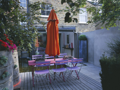 Small Courtyard Garden With Pink Wooden Table, Orange Parasol, Decking And Orange Cannas by Clive Nichols Pricing Limited Edition Print image