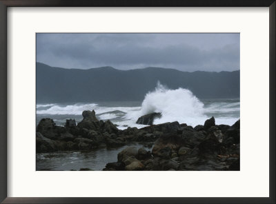 Waves Crashing Upon Rocks With Mountains In Background On Cloudy Day by Todd Gipstein Pricing Limited Edition Print image