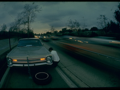 Man Changing Tire On Service Pull Off With Scant Space And Cars Whizzing By On Pasadena Freeway by Ralph Crane Pricing Limited Edition Print image