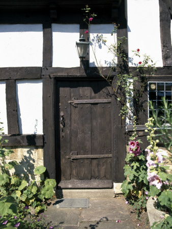 Doors - Half-Timbered Cottage- Wooden Door And Iron Hinges, Approached By Flagstone, Hollyhocks by David Mark Soulsby Pricing Limited Edition Print image