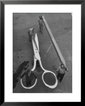 Stagehands Pushing A Pair Of Gigantic Scissors On A Dollie Next To Two Men Carrying A 21 Ft. Pencil by Allan Grant Pricing Limited Edition Print image