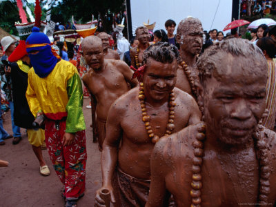 Men Dressed In Mud, Mandarin Orange Necklaces And Bamboo Staffs At Phi Ta Khon Festival, Thailand by Joe Cummings Pricing Limited Edition Print image