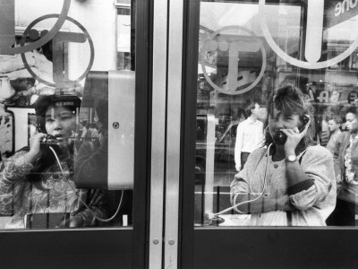 Two Women Make Calls From Phoneboxes - Oxford Street, London by Shirley Baker Pricing Limited Edition Print image