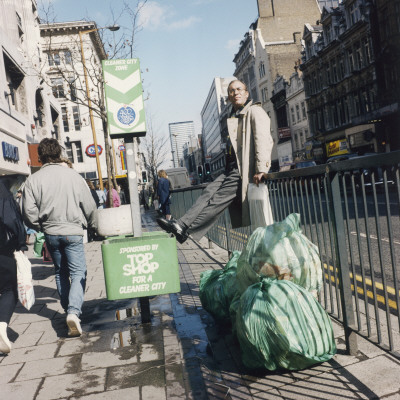 Man On A Streetside Fence By Some Rubbish by Shirley Baker Pricing Limited Edition Print image