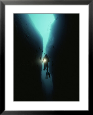 A Diver Swims Through A Large Crack In The Rock Of Tgyiani Reef by Bill Curtsinger Pricing Limited Edition Print image
