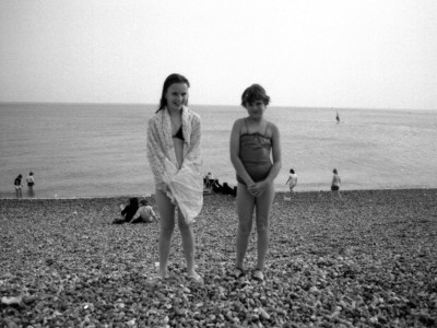 Two Little Girls Pose For Their Photo On A Pebbly Brighton Beach by Vanessa Wagstaff Pricing Limited Edition Print image
