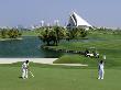 Men On Dubai Creek Golf With Yacht Club In Distance, Dubai, United Arab Emirates by Holger Leue Limited Edition Print