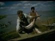 Fisherman Hefting Osetra Sturgeon Caught Sweep Netting Into Boat In Volga River Delta, Russia by Carl Mydans Limited Edition Print