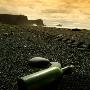 A Green Bottle Lying On A Beach, Cliff Dyrholaey In Background, South Iceland by Larus Karl Ingasson Limited Edition Print