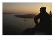A Silhouetted Greek Man Enjoys A Sunset From A High Point On Thira by Tino Soriano Limited Edition Print