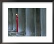 Carnival Model In Red Cape And Gold Mask Peering From Columns In St. Mark's Square, Veneto, Italy by Lee Frost Limited Edition Print
