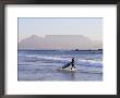 Young Woman Surfer Enters The Water Of The Atlantic Ocean With Table Mountain In The Background by Yadid Levy Limited Edition Pricing Art Print