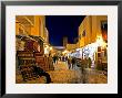 People Strolling Along Cobblestone Street Past Carpet Seller At Twilight, Kairouan, Tunisia by Bethune Carmichael Limited Edition Print