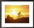 A Woman Rides Her Bike In The Sunset With Rock Cliffs In The Background by Dugald Bremner Limited Edition Print