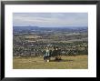 Three Girls Sitting On Bench Looking At View Over Bishops Cleeve Village, The Cotswolds, England by David Hughes Limited Edition Pricing Art Print