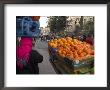 Palestinian Woman In Colourful Scarf And Carrying Bag On Her Head Walking Past An Orange Stall by Eitan Simanor Limited Edition Print