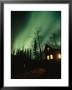 Aurora Borealis Fills The Sky Over A Warmly Lit Cabin by Rich Reid Limited Edition Print